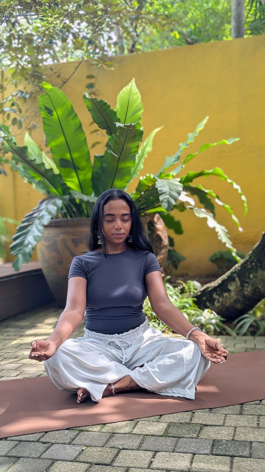 A woman meditating beside tropical plants at Svastha Studio
